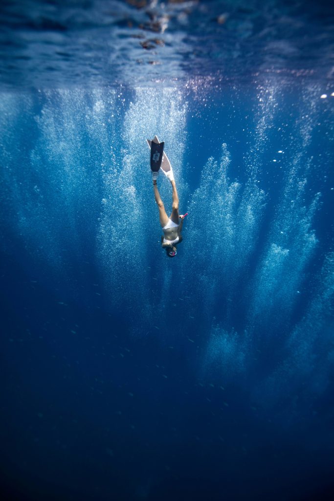 A person swims underwater, holding a surfboard