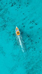 Aerial view of a small boat with an orange roof gliding through vibrant turquoise